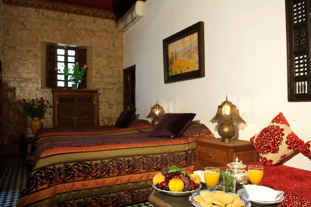 A traditional room with a bed, a table with fruit and drinks, and a decorative lamp.