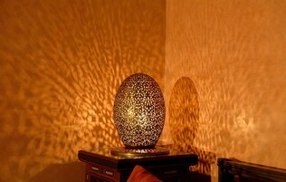 Uma lâmpada esférica, com padrão intrincado, sobre uma mesa de madeira em frente a uma parede texturizada.
