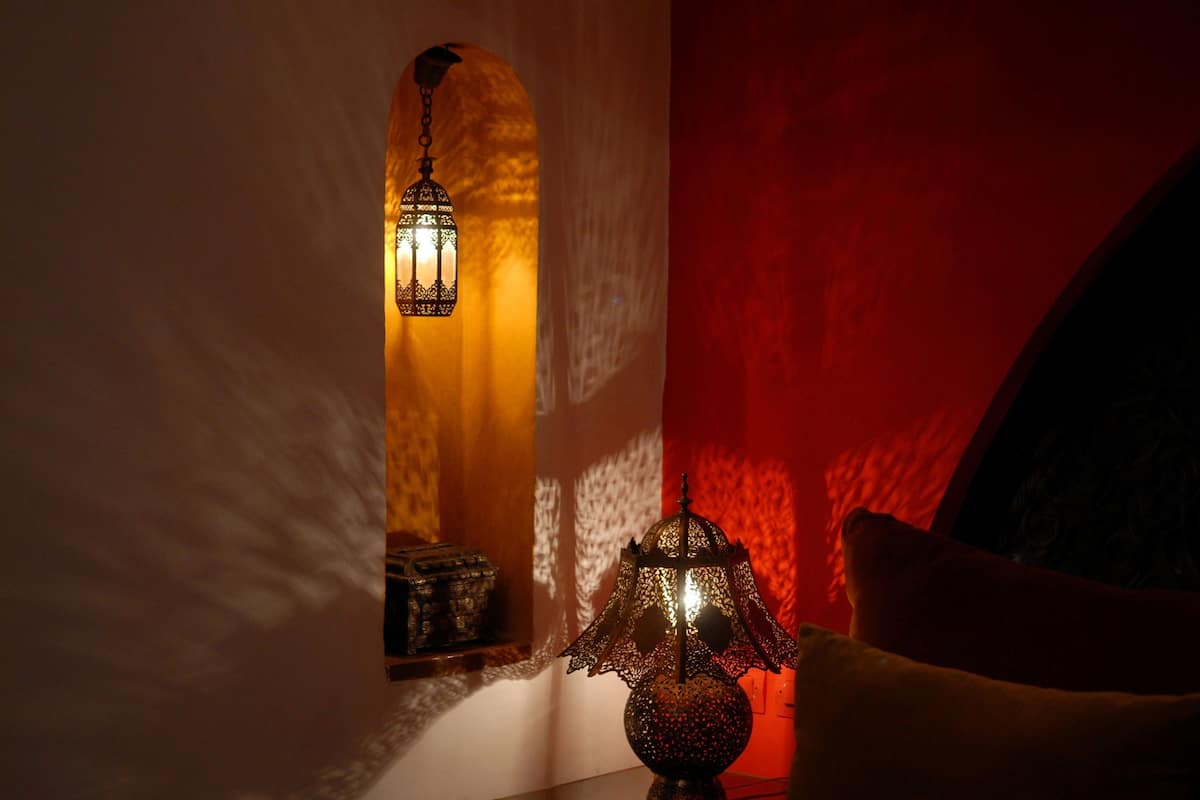 A room with a wall-mounted lamp casting a warm glow, a small decorative item on a shelf, and a red accent wall.