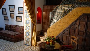 A room with a checkered floor, a sofa, a table with fruit, a staircase with a metal railing, and patterned walls. - Dar Tazi - Medina View (Fes)