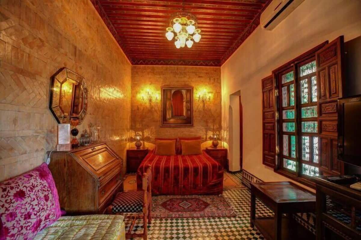 A traditional room with a bed, wooden furniture, a patterned rug, and a chandelier.
