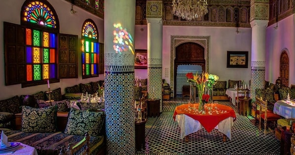 Una habitación con cojines estampados, una mesa con mantel rojo y una araña.