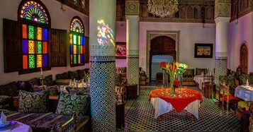 Um quarto com almofadas estampadas, uma mesa com toalha vermelha e um candelabro.
