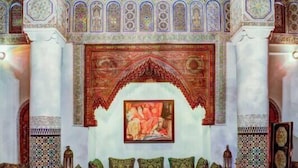 A traditional Moroccan interior with a patterned floor, a sofa set, and a large painting on the wall. - Dar Tazi - Medina View (Fes)