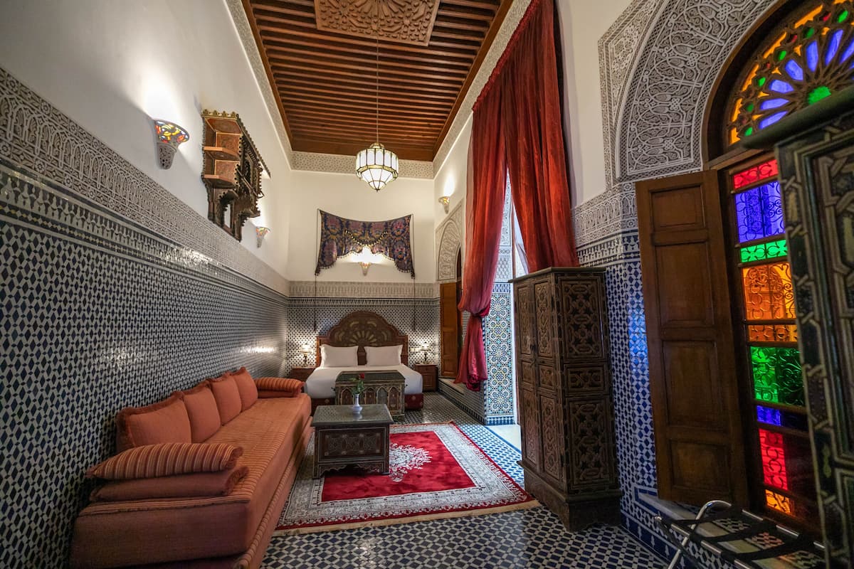 A Moroccan-style room with a patterned wall, a sofa, a bed, and a decorative wooden cabinet.