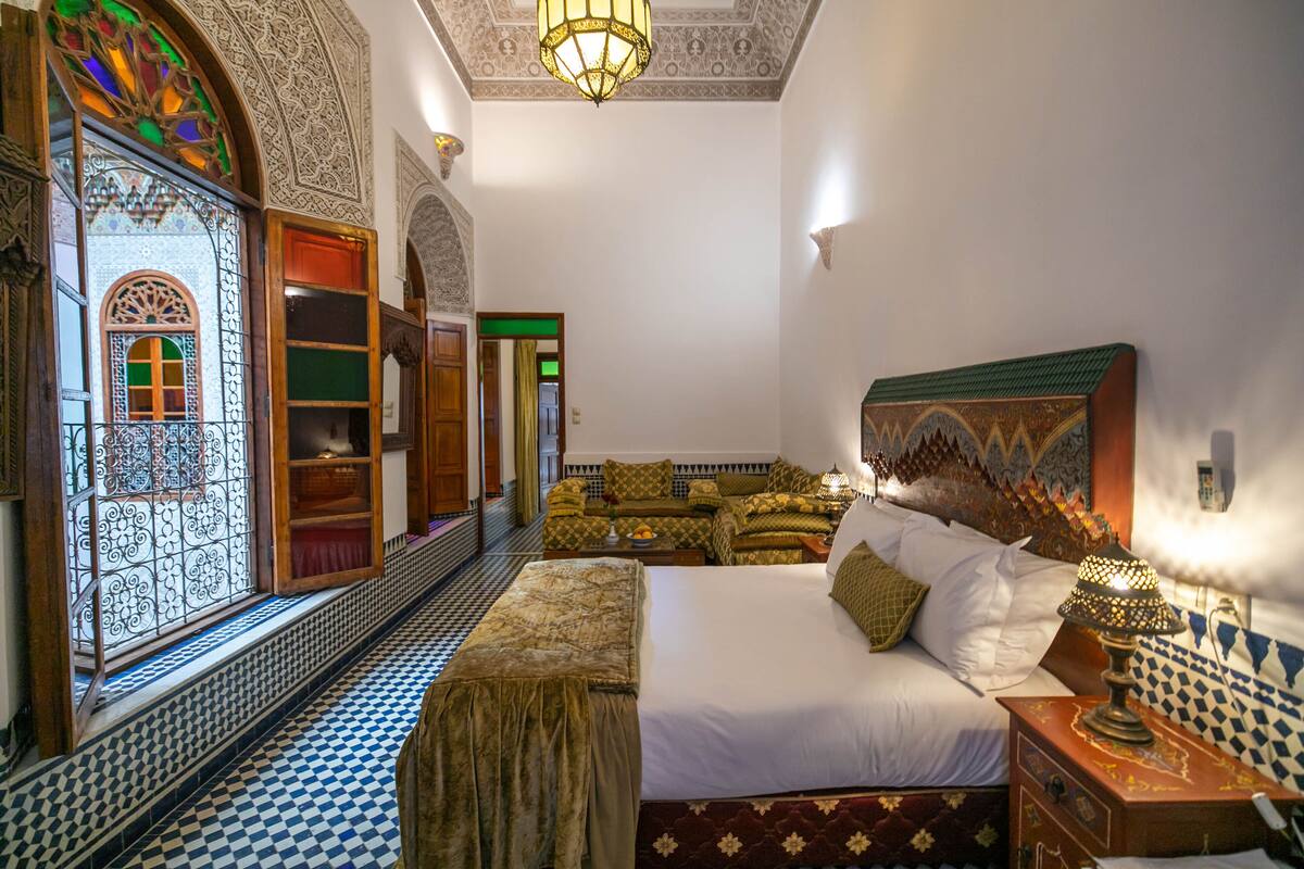 A traditional Moroccan room with a large bed, ornate wooden furniture, and patterned tile flooring.