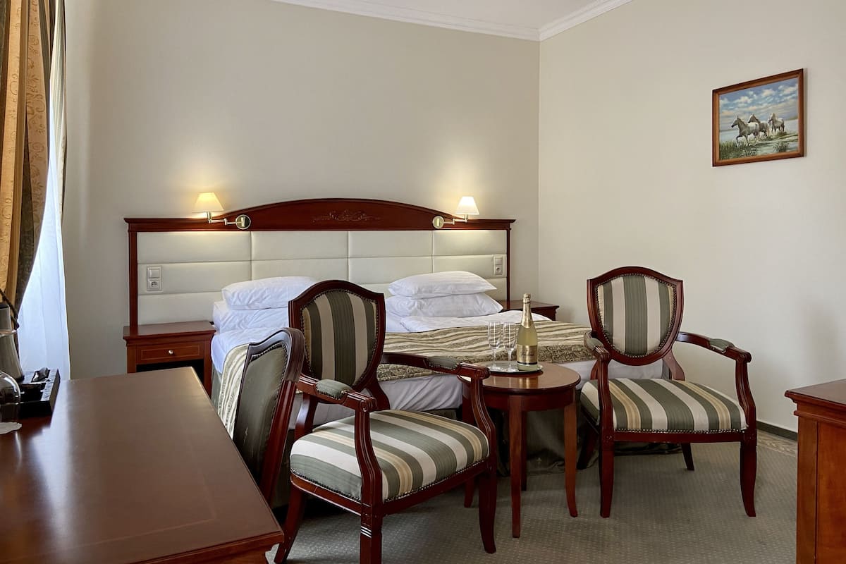 A hotel room with a large bed, two upholstered chairs, a small table, and a painting on the wall.