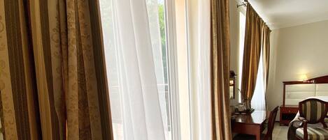 A hotel room with a large window, a wooden bench, a dining table, and a chair.