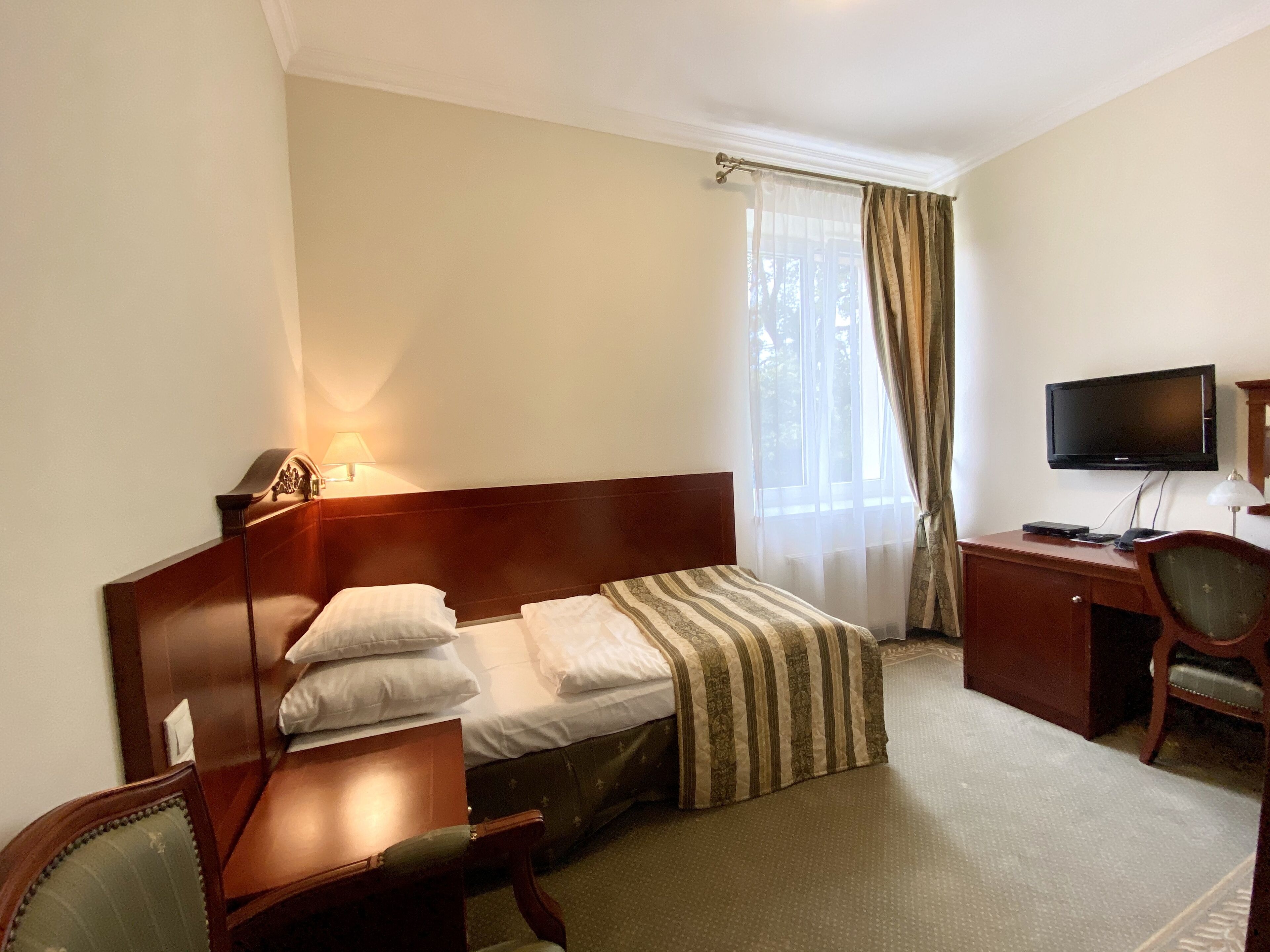 A hotel room with a bed, a desk, a chair, a television, and a window with curtains.