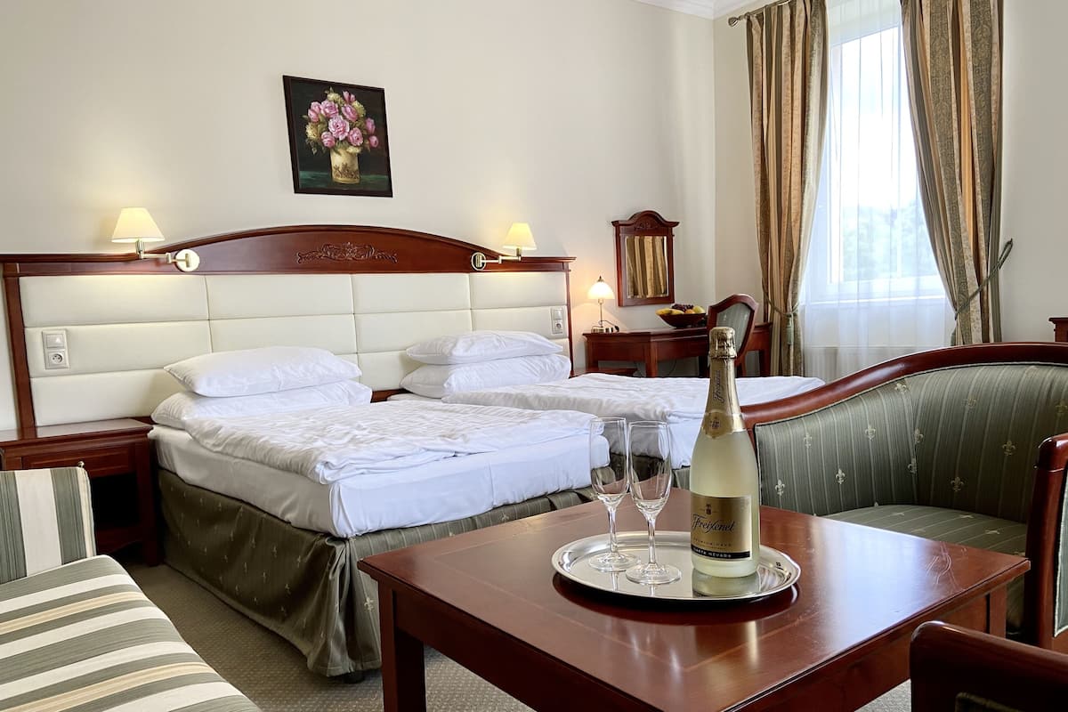 A hotel room with two beds, a dining table with a bottle of champagne, and a chair.