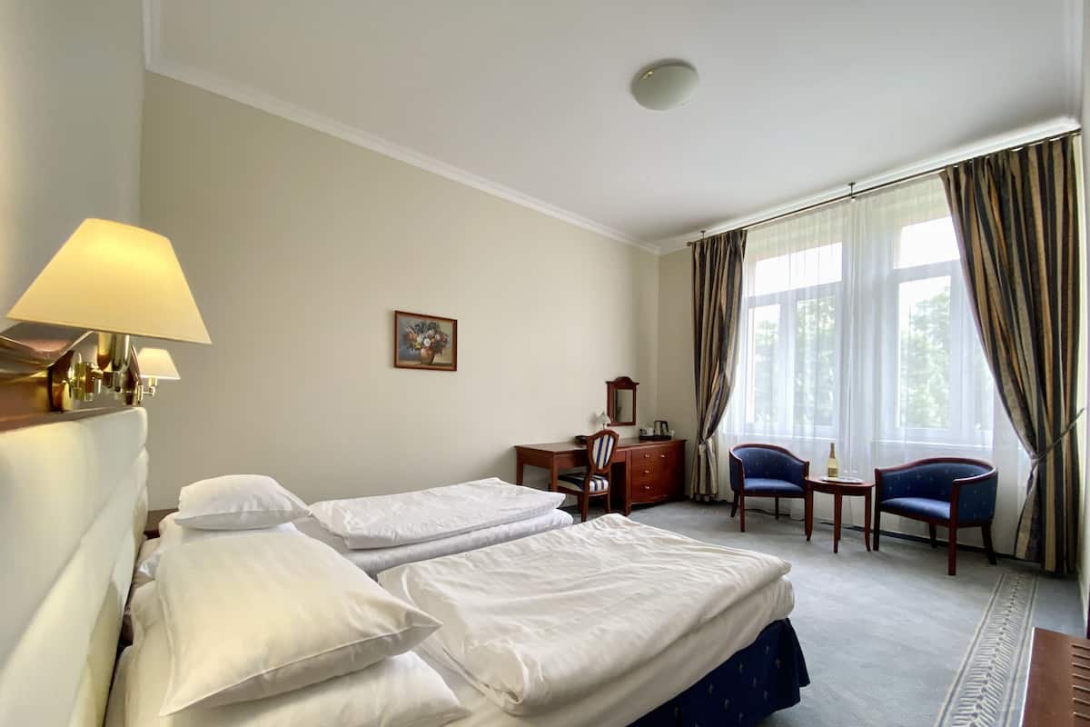 A hotel room with two beds, a desk, a chair, a lamp, and a window with curtains.