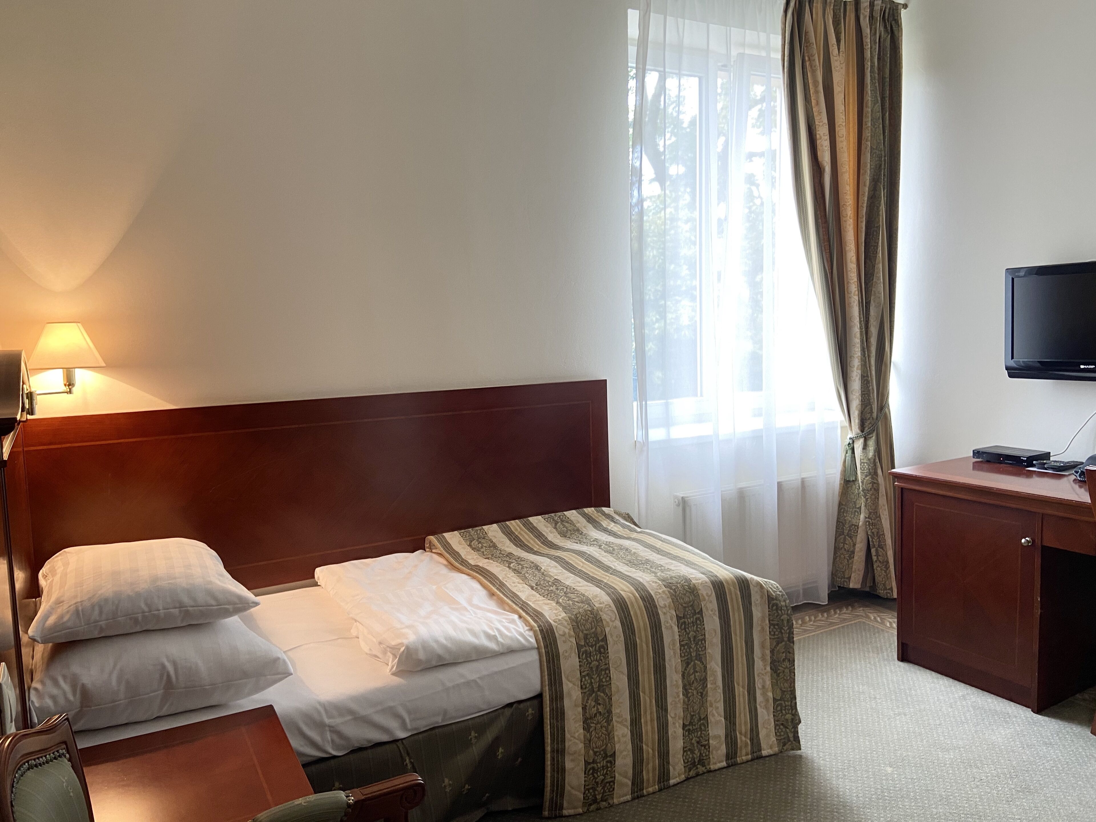 A hotel room with a bed, a desk, a television, and a window with curtains.