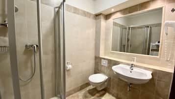 A bathroom with a glass shower enclosure, a toilet, and a sink with a mirror above it.