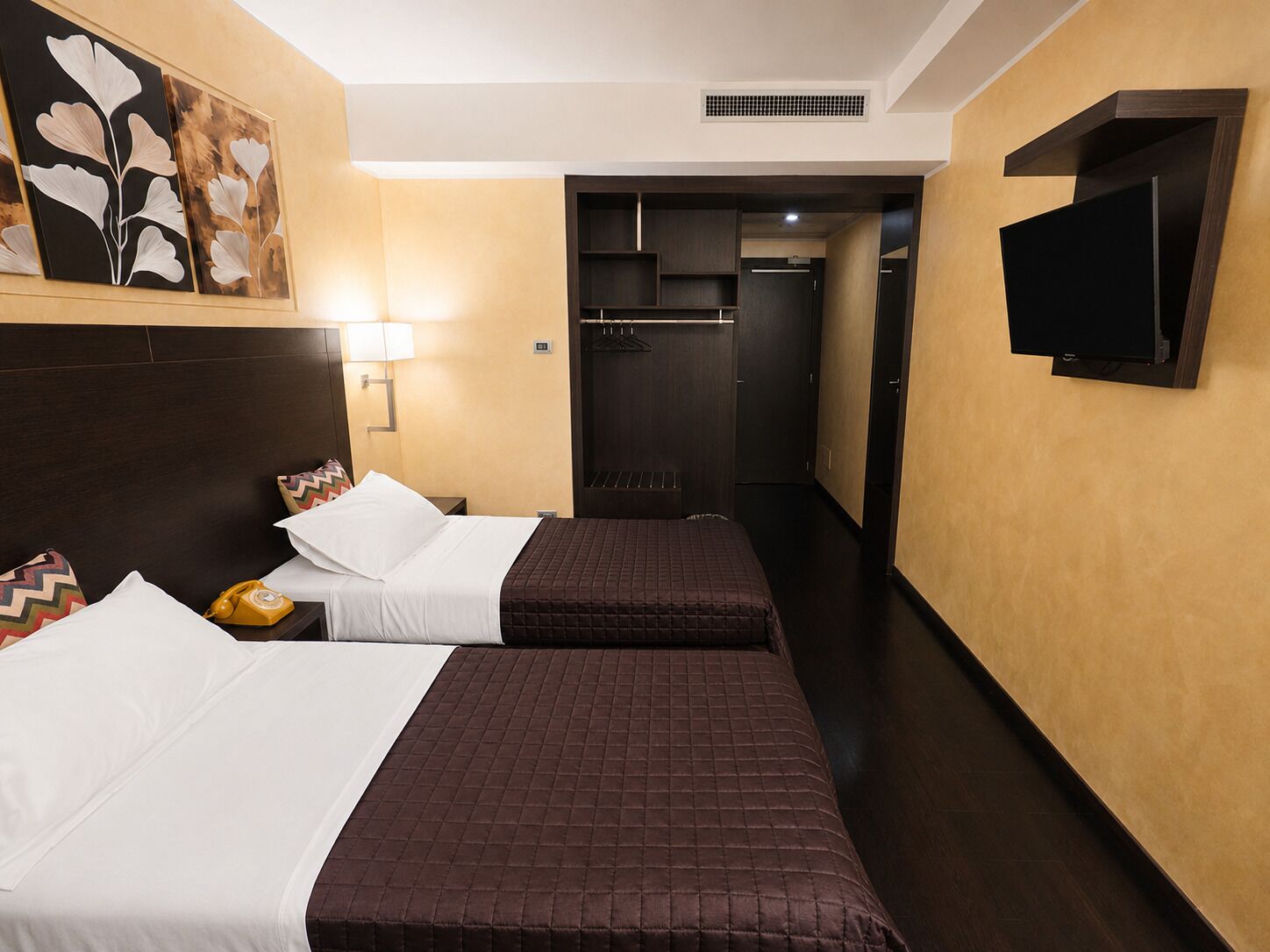 A hotel room with two beds, a television, a phone, and a painting on the wall.