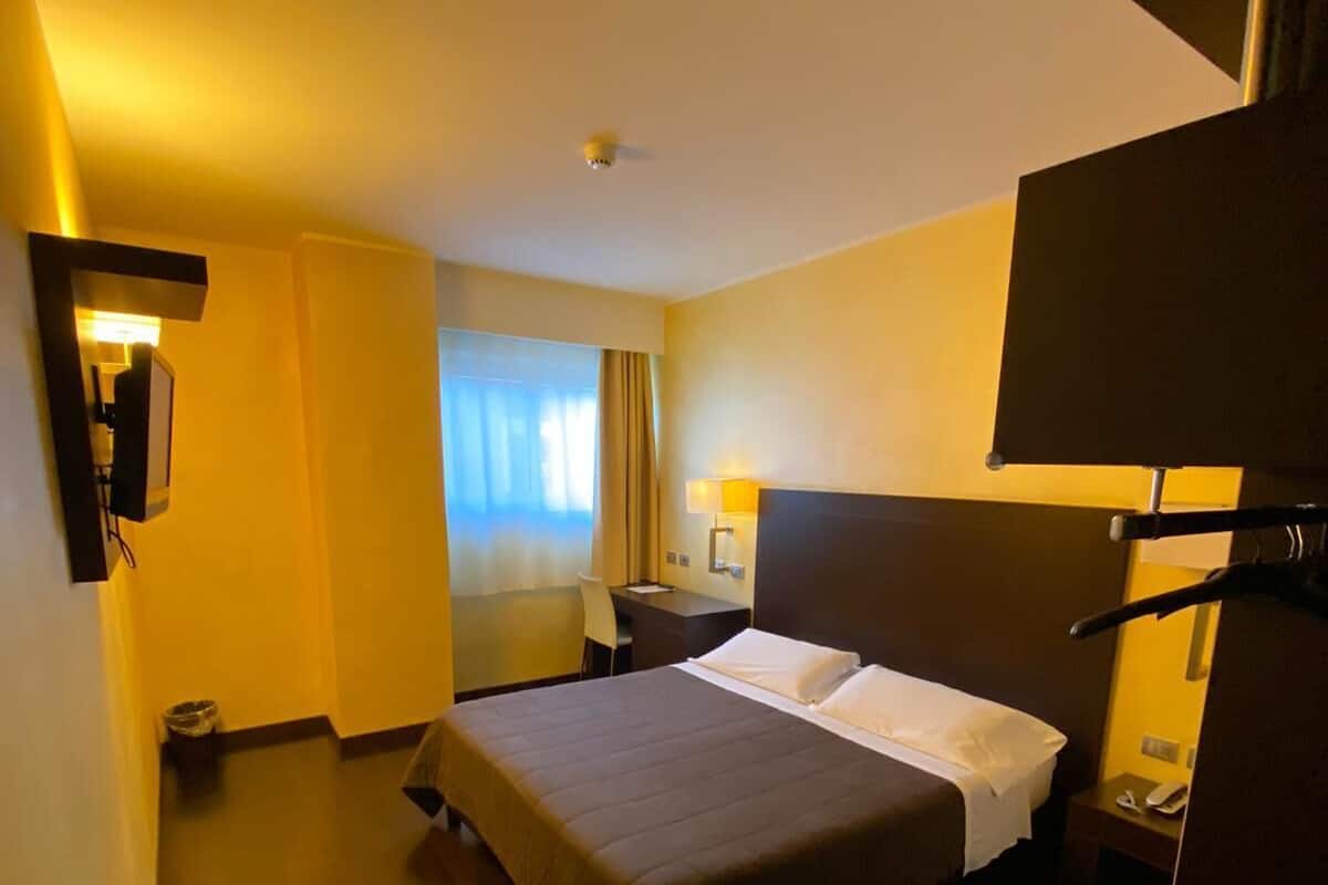 A hotel room with a large bed, a desk, a chair, a lamp, and a window with curtains.