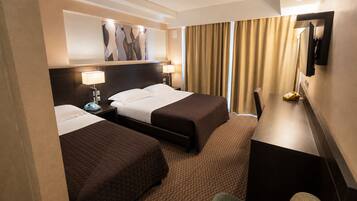 A hotel room with two beds, a desk, a chair, a telephone, and a painting on the wall.