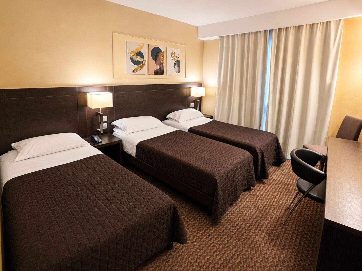 Een hotelkamer met twee bedden, een bureau en een stoel. Boven de bedden hangt een schilderij.