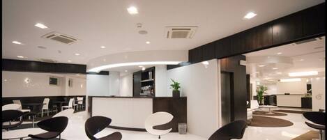 Um saguão moderno com um balcão de recepção curvo, áreas de estar com cadeiras contemporâneas e um espaço limpo e bem iluminado.