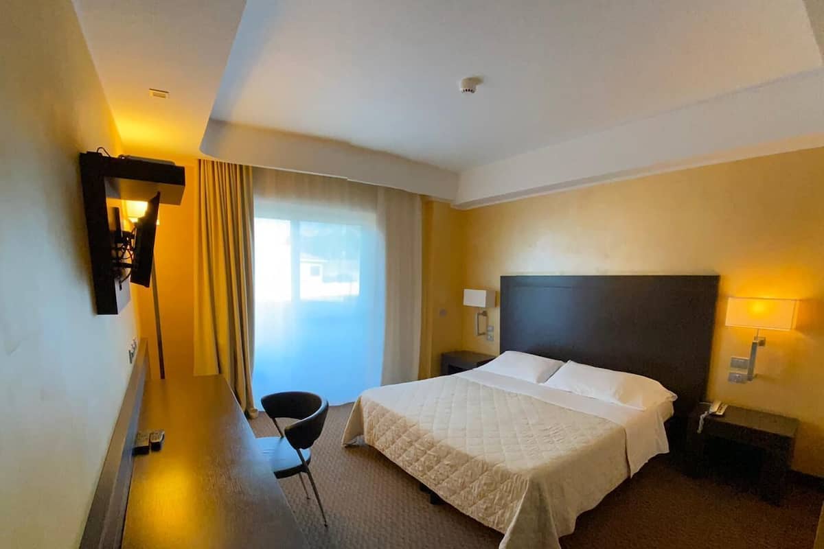 A hotel room with a large bed, a desk, a chair, and a TV mounted on the wall.