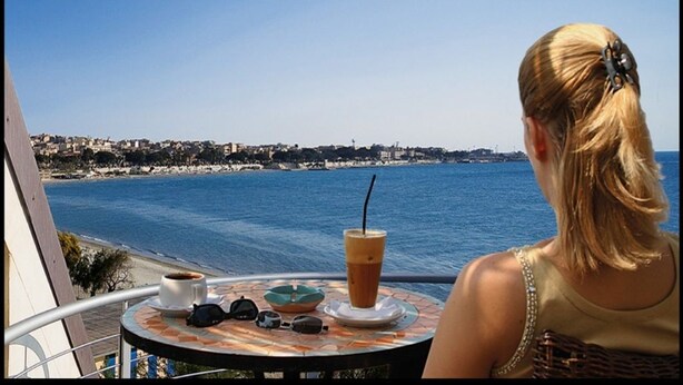 Un balcon avec une table, une boisson et des lunettes de soleil.
