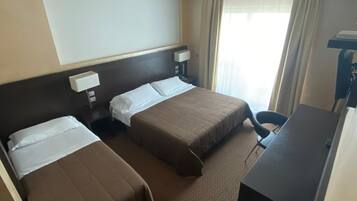 Habitación de hotel con dos camas, un escritorio, una silla, un televisor de pantalla plana y un detector de humo en el techo.