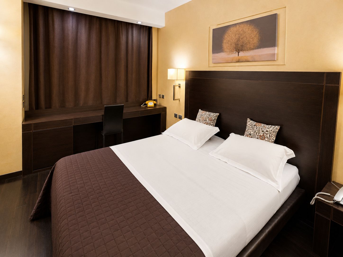 Una habitación de hotel con una cama grande, un escritorio con teléfono, una silla y una lámpara de pared.