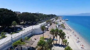 Une zone côtière avec une plage, des palmiers et un grand bâtiment doté d’un toit incurvé.