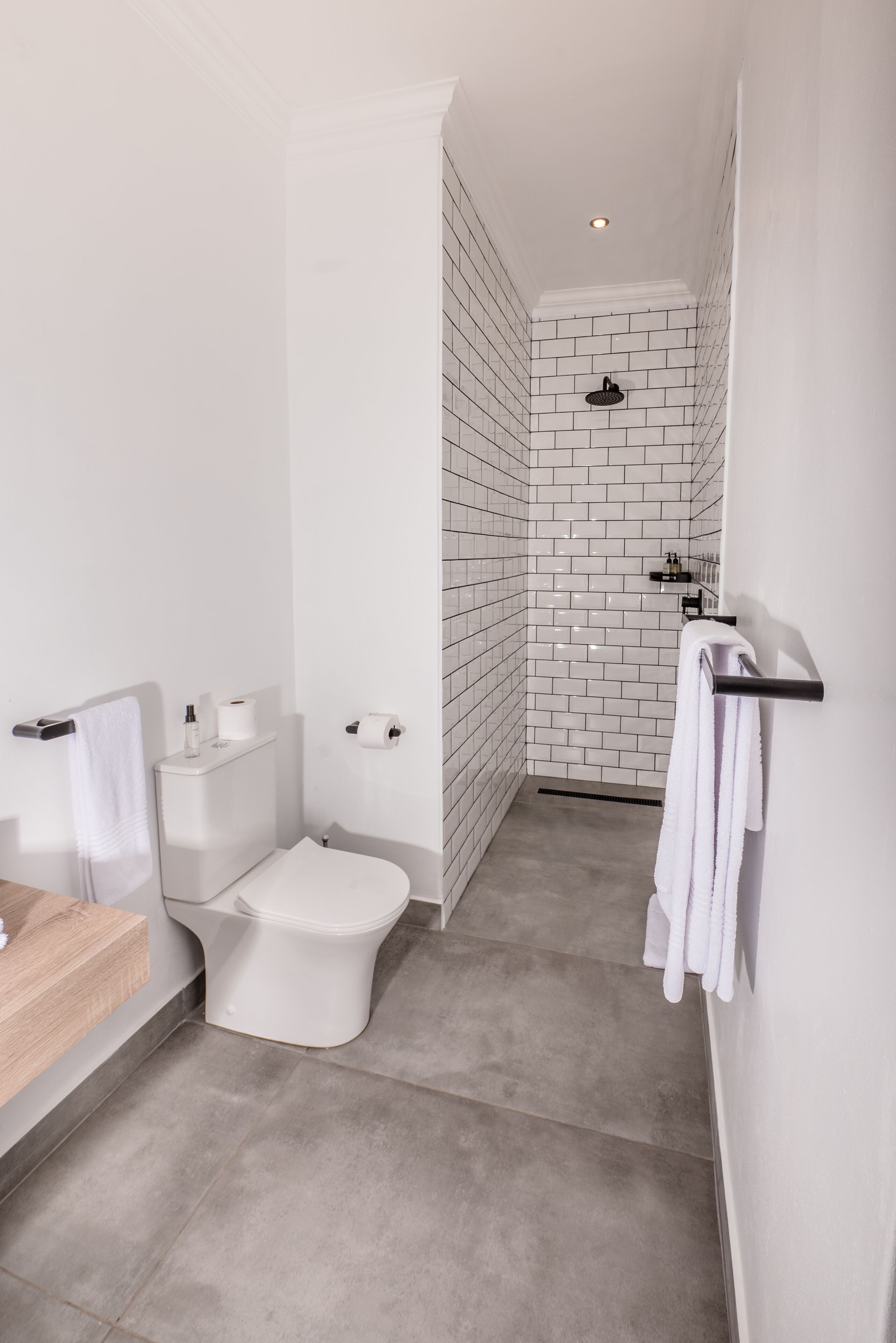 A modern bathroom with a white toilet, a shower area with a black showerhead, and a towel rack.