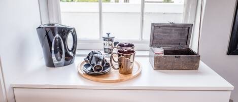 A white desk with a coffee maker, a mug, a tray, and a wooden box.