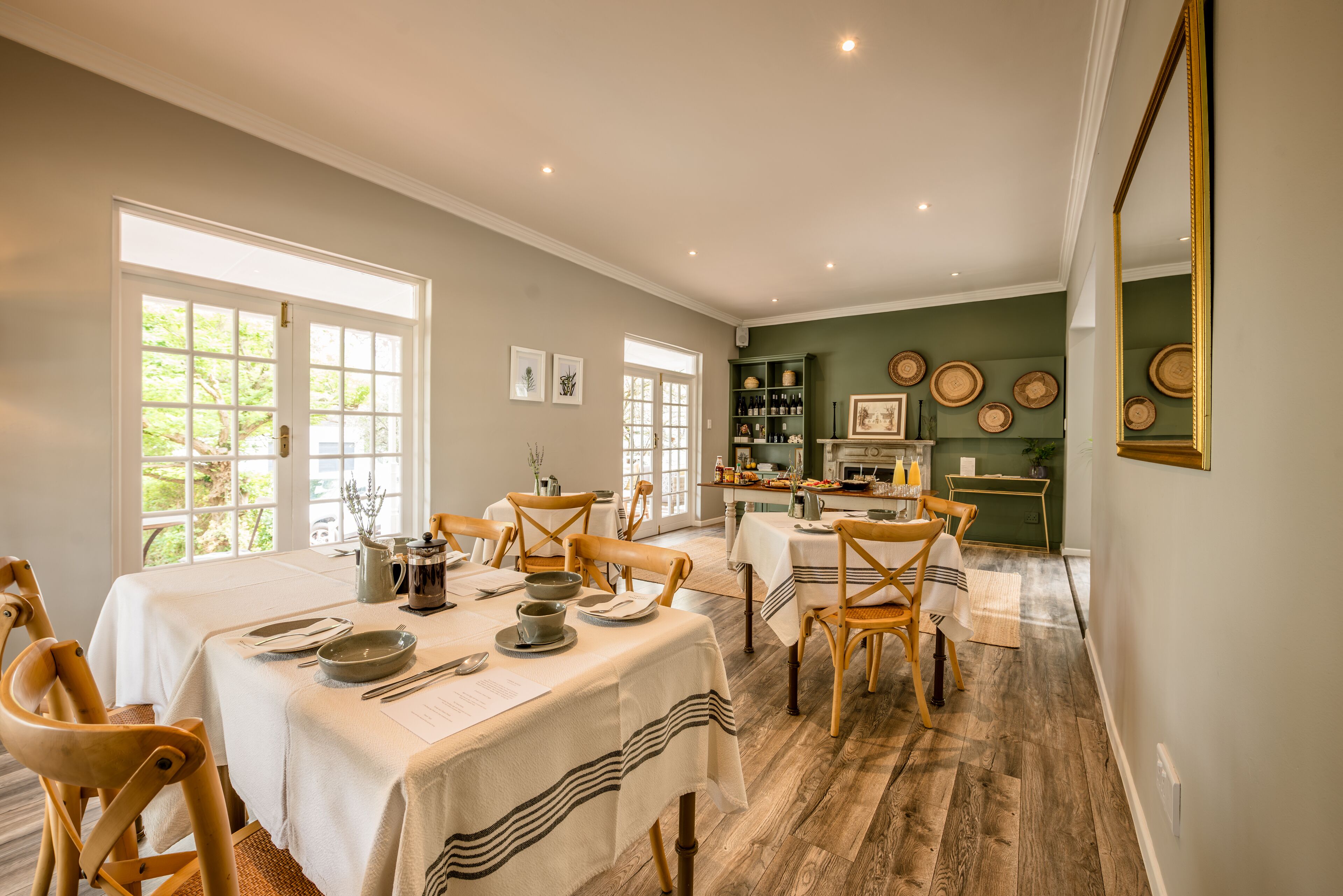 A dining area with a long table set for a meal, wooden chairs, and a kitchen in the background.