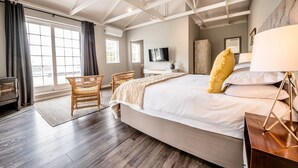 Een ruime slaapkamer met een groot bed, een aan de muur bevestigde televisie en een houten balkenplafond.