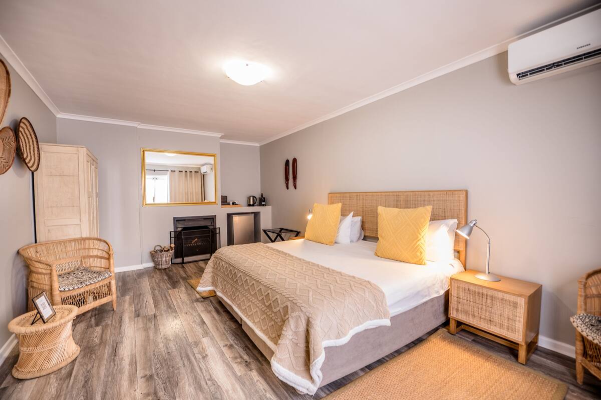 A bedroom with a large bed, bedside tables, a wicker chair, a mirror, and a fireplace.