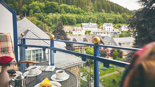 Un balcón con una mesa dispuesta para dos, con vistas a una colina con edificios y árboles.