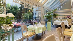 Un comedor interior con mesas dispuestas para una comida, rodeado de paredes de vidrio con vistas al exterior.