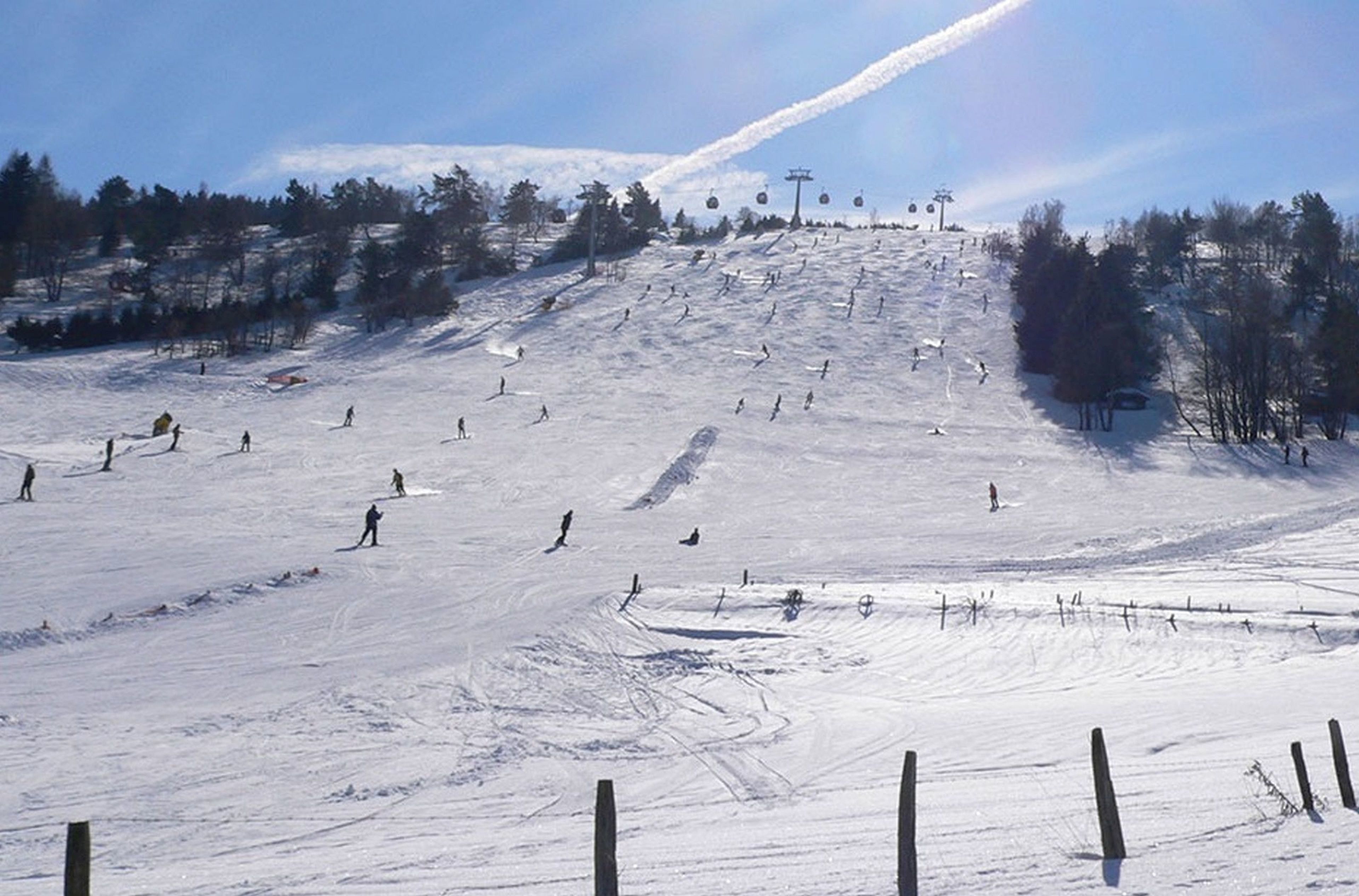 A ski slope with skiers and a ski lift in the background.