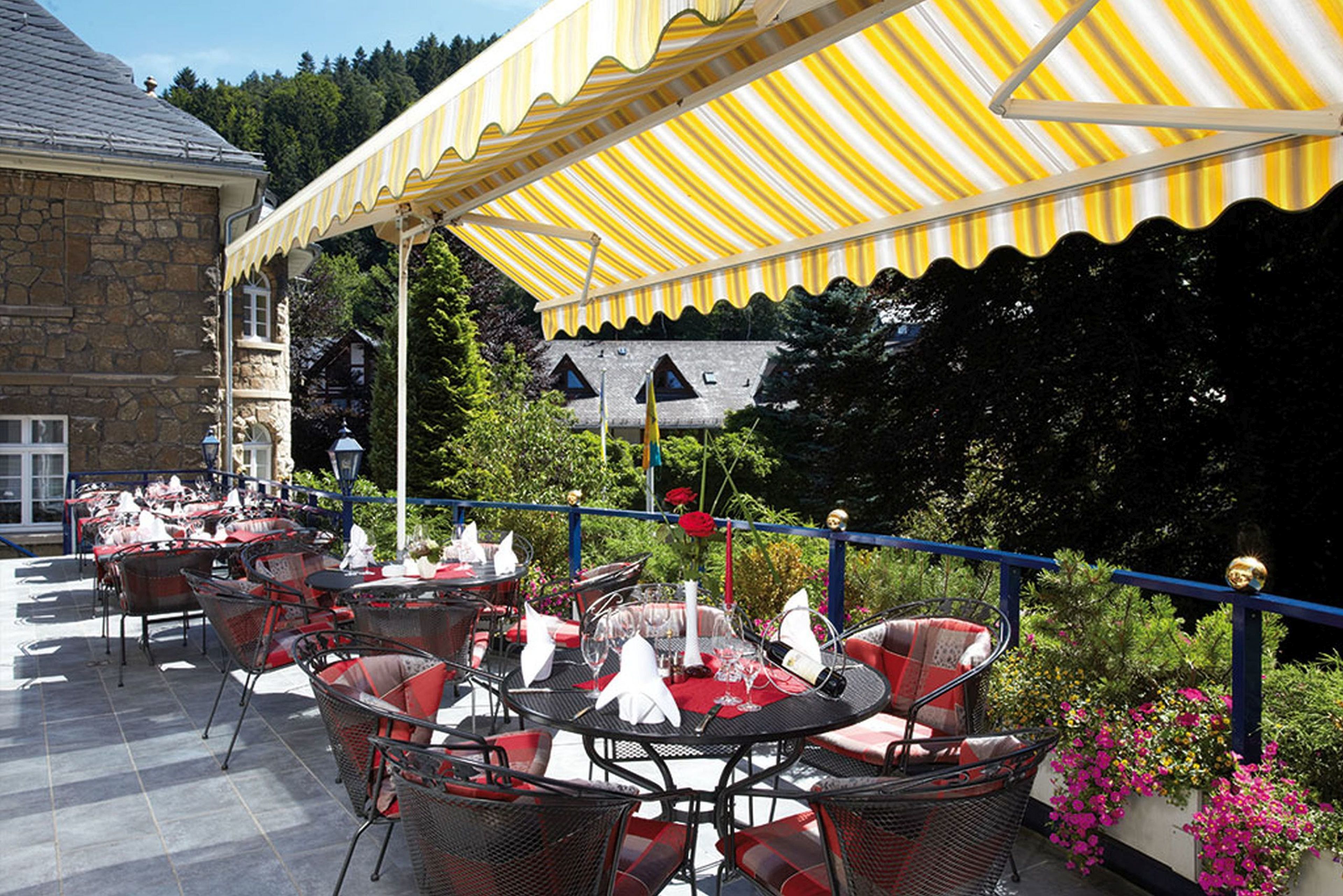 An outdoor patio with tables and chairs, a yellow striped awning, and a stone building in the background.