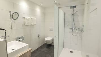 Un baño moderno con ducha de vidrio, lavamanos blanco y retrete.