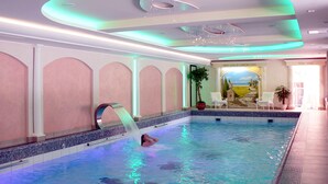 Una piscina interior con tobogán de agua, un mural y una zona de estar con sillas.