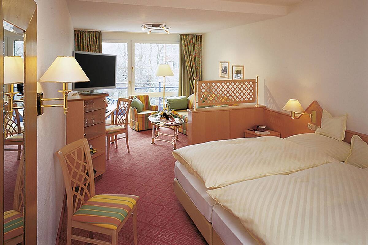 A hotel room with a large bed, a television, a desk with a lamp, a chair, and a window with curtains.