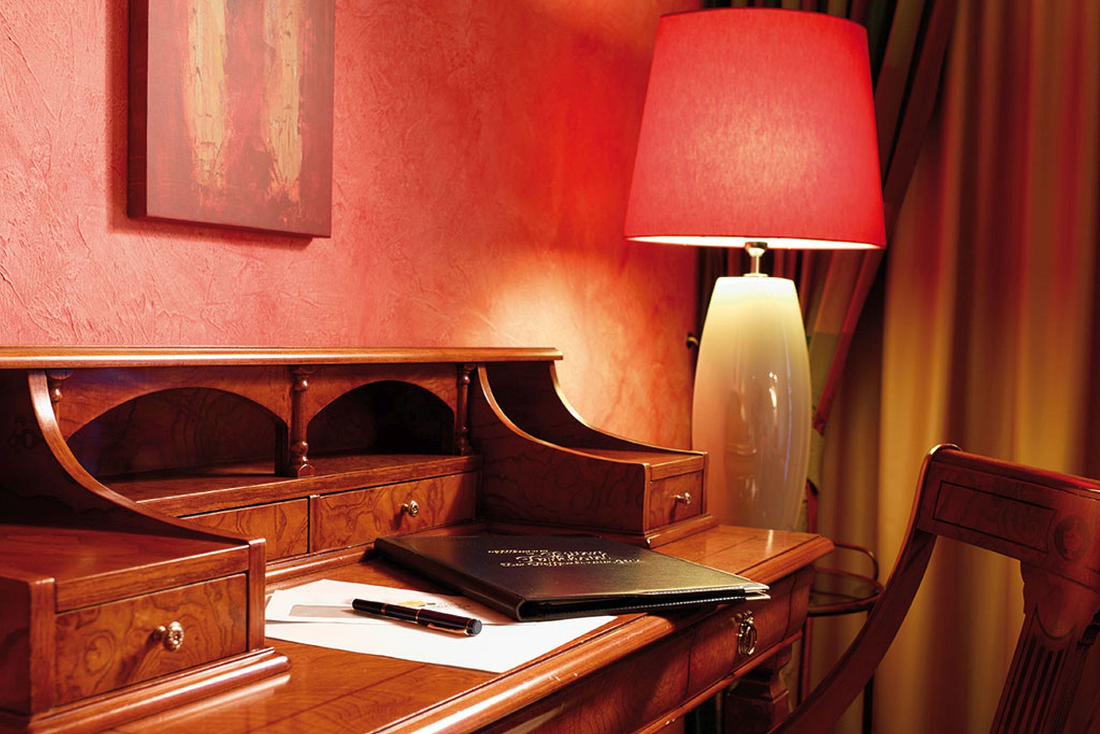 A wooden desk with a laptop, a pen, and a red lamp.