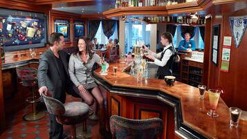 A bar area with wooden furniture, a bartender, and a television screen.