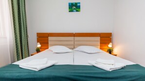Cama doble con cabecera de madera, dos mesitas de noche con lámparas y colcha verde.