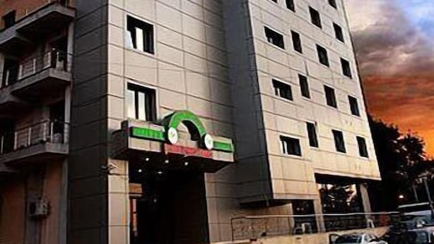 Un edificio de varios pisos con un diseño arquitectónico moderno, que presenta una entrada destacada con un letrero verde y blanco.