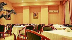 Un salón de conferencias con varias mesas y sillas, un cuadro en la pared y una planta en maceta.