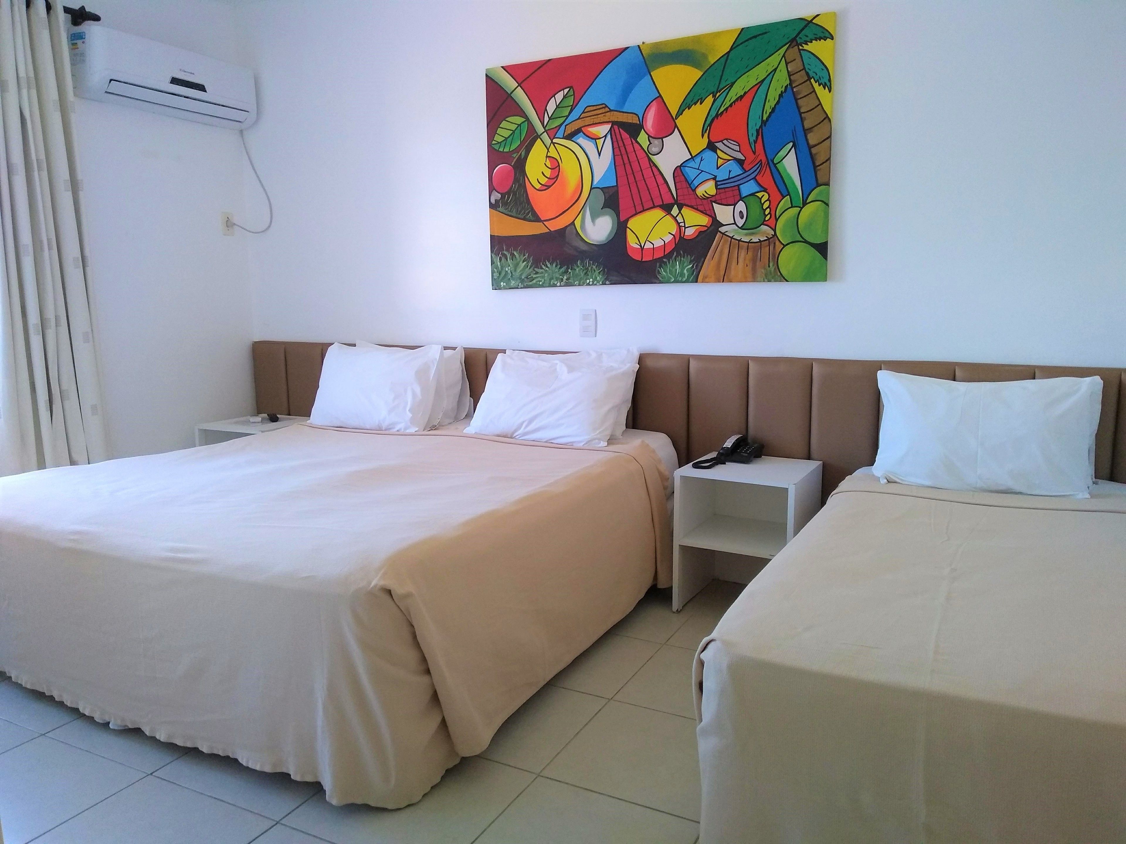 A hotel room with a large bed, two bedside tables, a nightstand, and a colorful abstract painting on the wall.