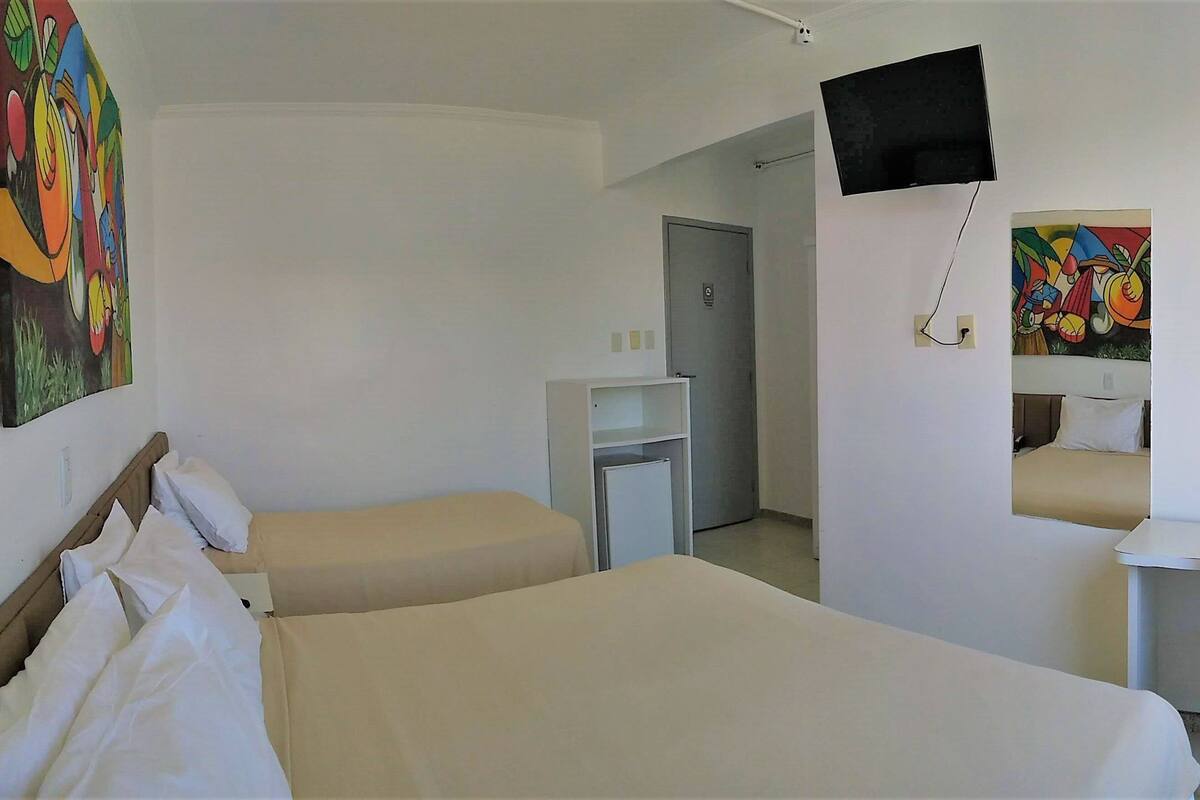 A hotel room with two beds, a desk, a chair, a TV, and artwork on the walls.