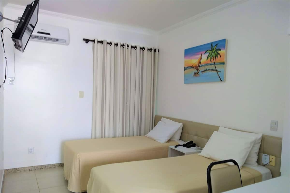 A hotel room with two beds, a TV mounted on the wall, a painting of a sunset, and a curtain.