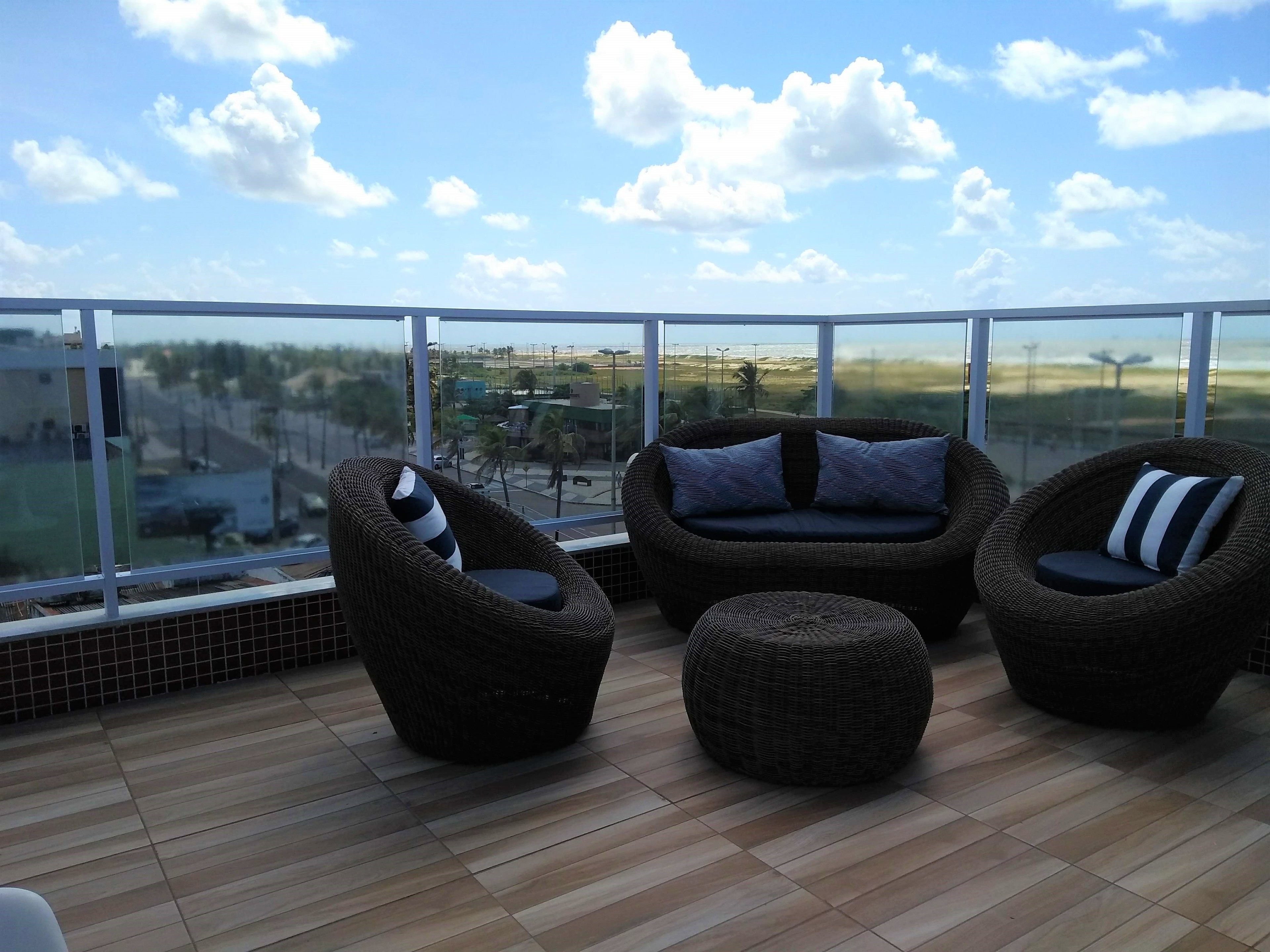 A balcony with wicker furniture and a glass railing overlooking a cityscape.