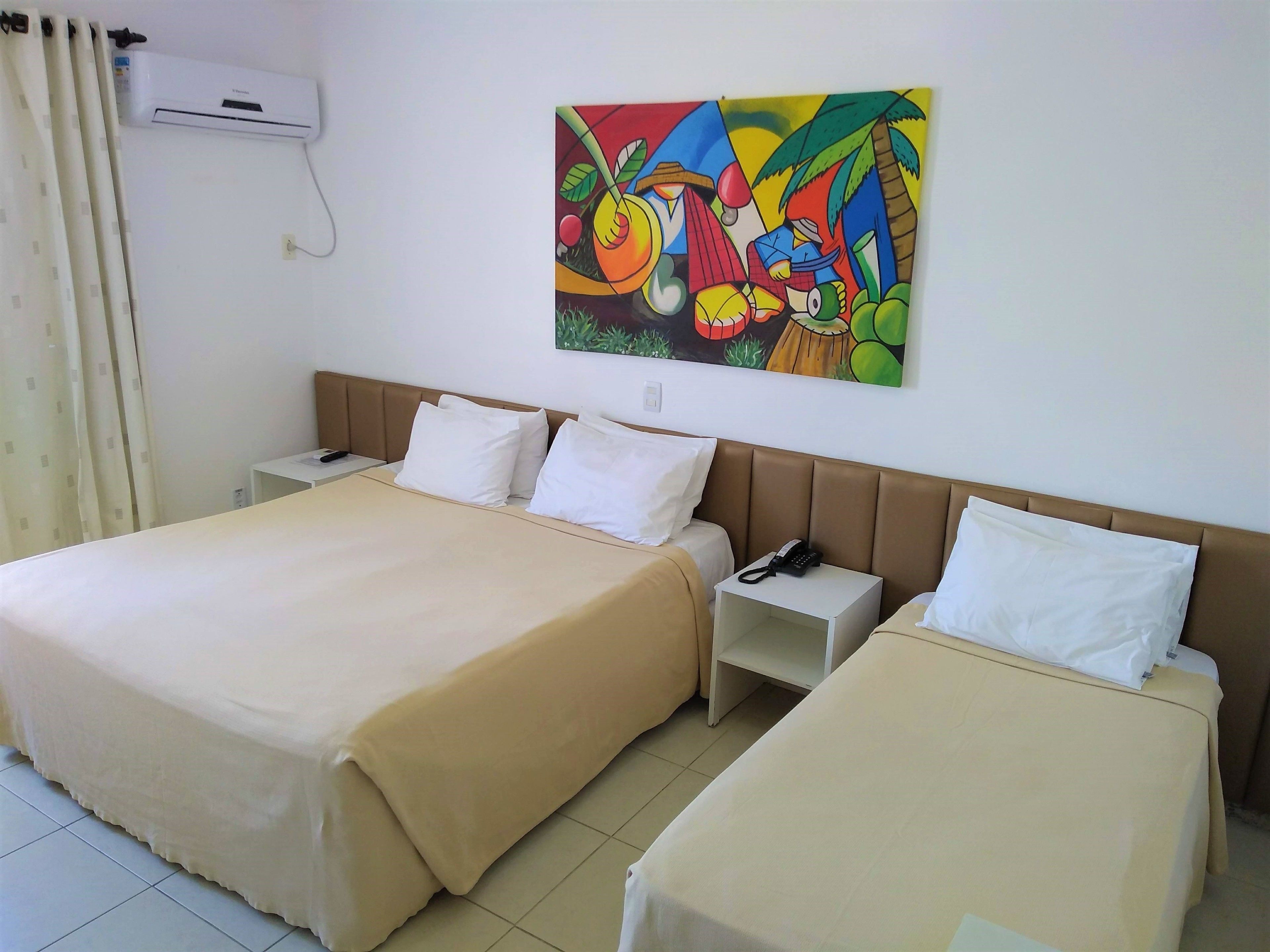 Una camera d'albergo con due letti, un comodino, un telefono e un quadro colorato appeso alla parete.