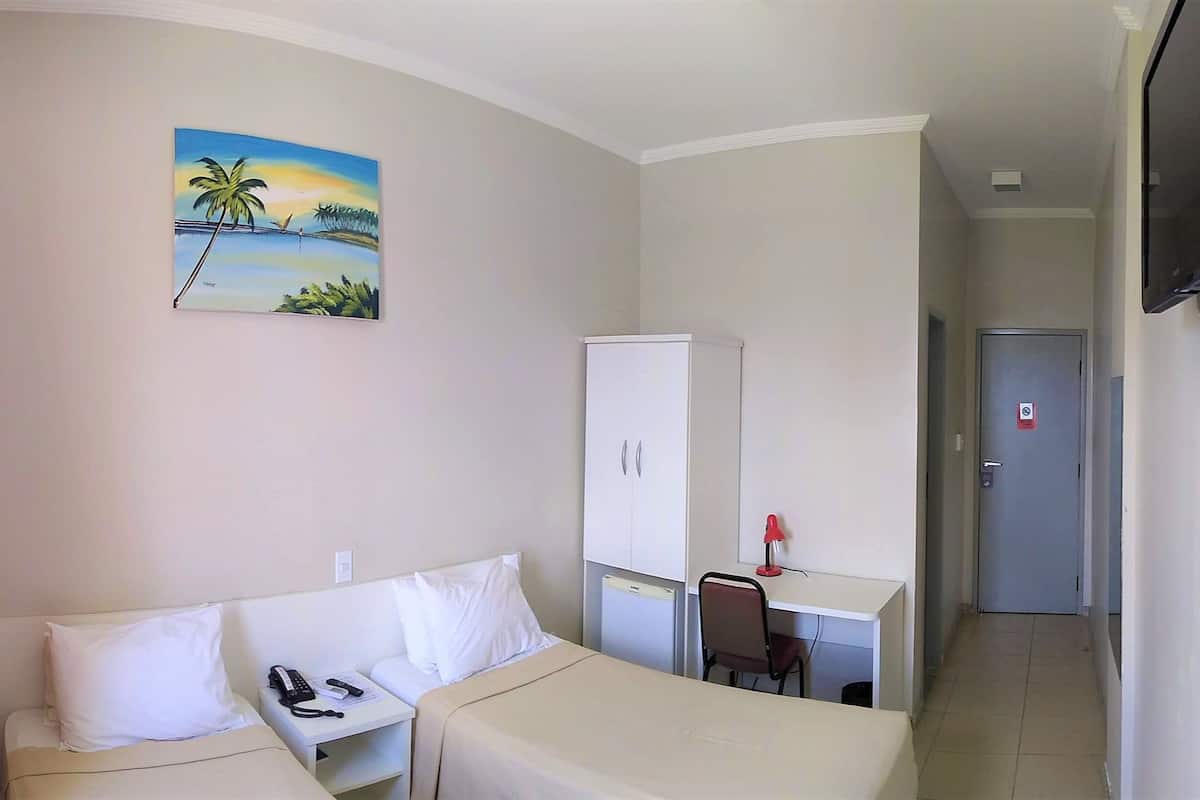 A hotel room with two beds, a desk, a chair, a TV, and a painting of a beach scene.